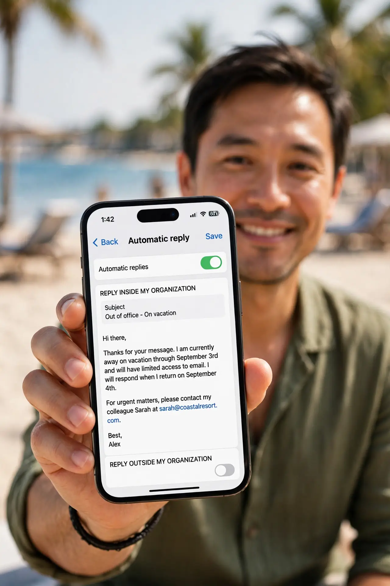 A relaxed adult on vacation holding a real phone showing an Outlook automatic reply being composed with legible text, beach blurred in background, the person's face content.